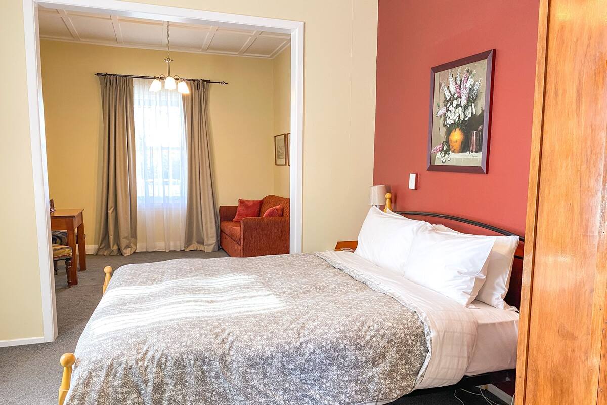 Een slaapkamer met een bed, een stoel, een tafel en een schilderij aan de muur.