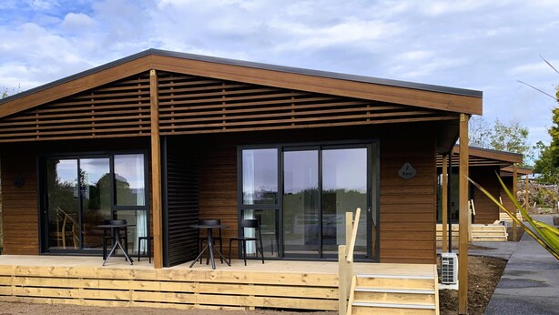 A modern wooden building with large sliding glass doors, a covered patio area, and a wooden deck. - Tongariro Crossing Lodge (National Park Village)