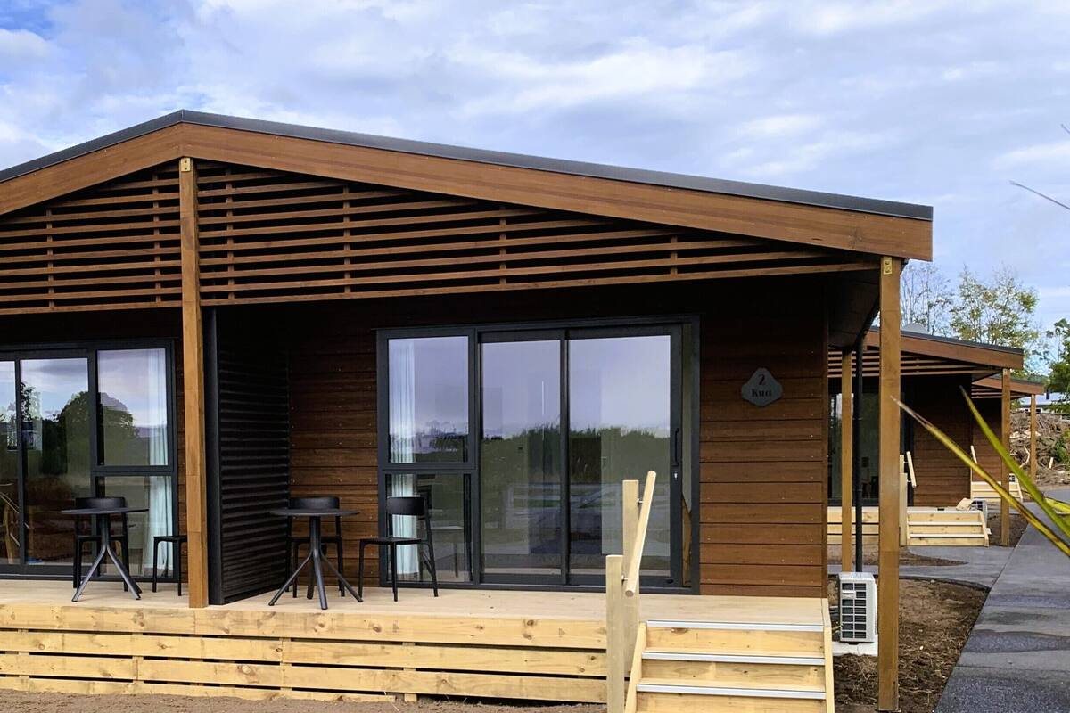 Een modern houten gebouw met grote schuifdeuren van glas, een overdekt terras en een houten terras.