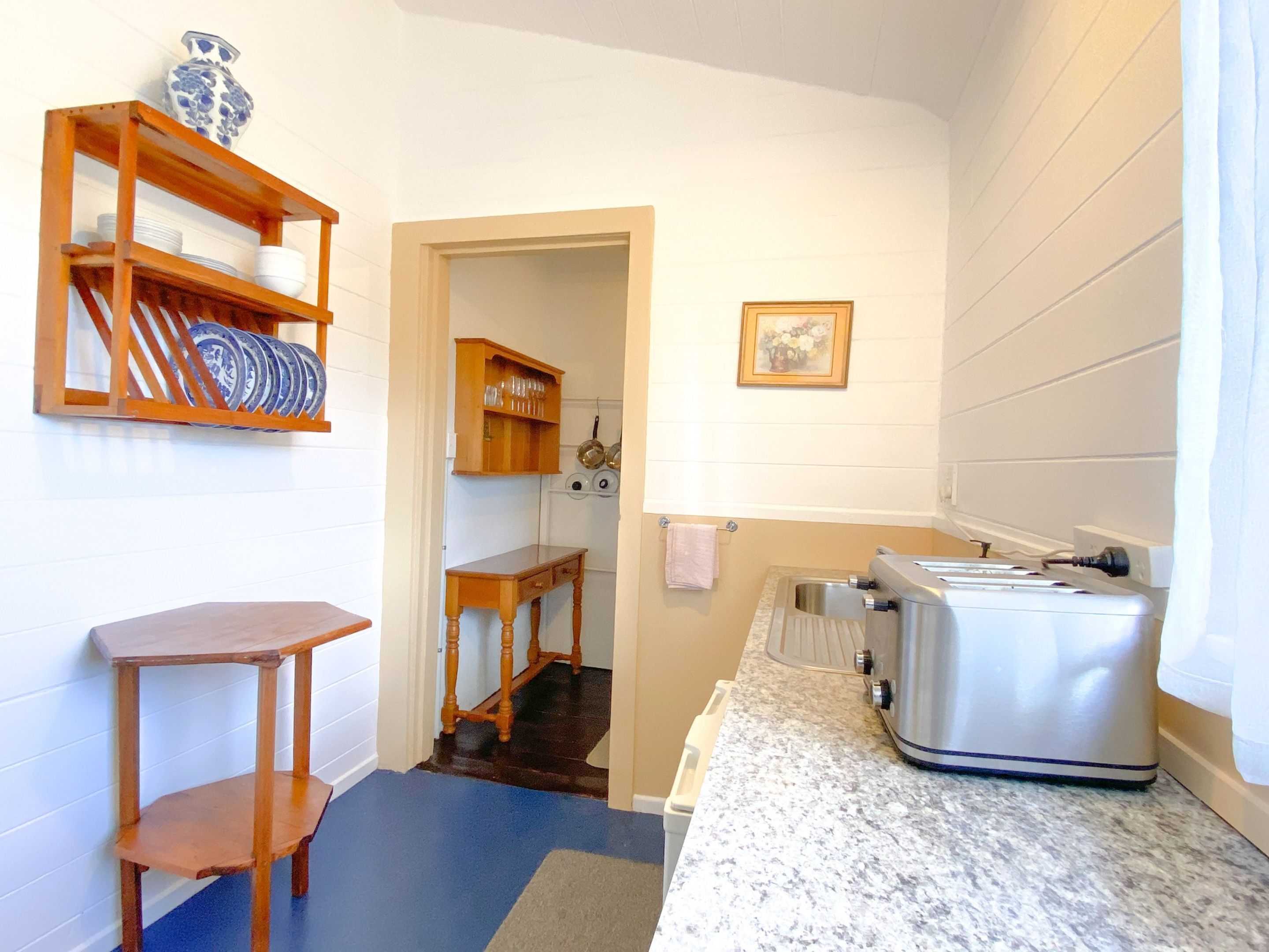 A compact kitchen with a granite countertop, a stainless steel toaster, and a wooden shelf with dishes.