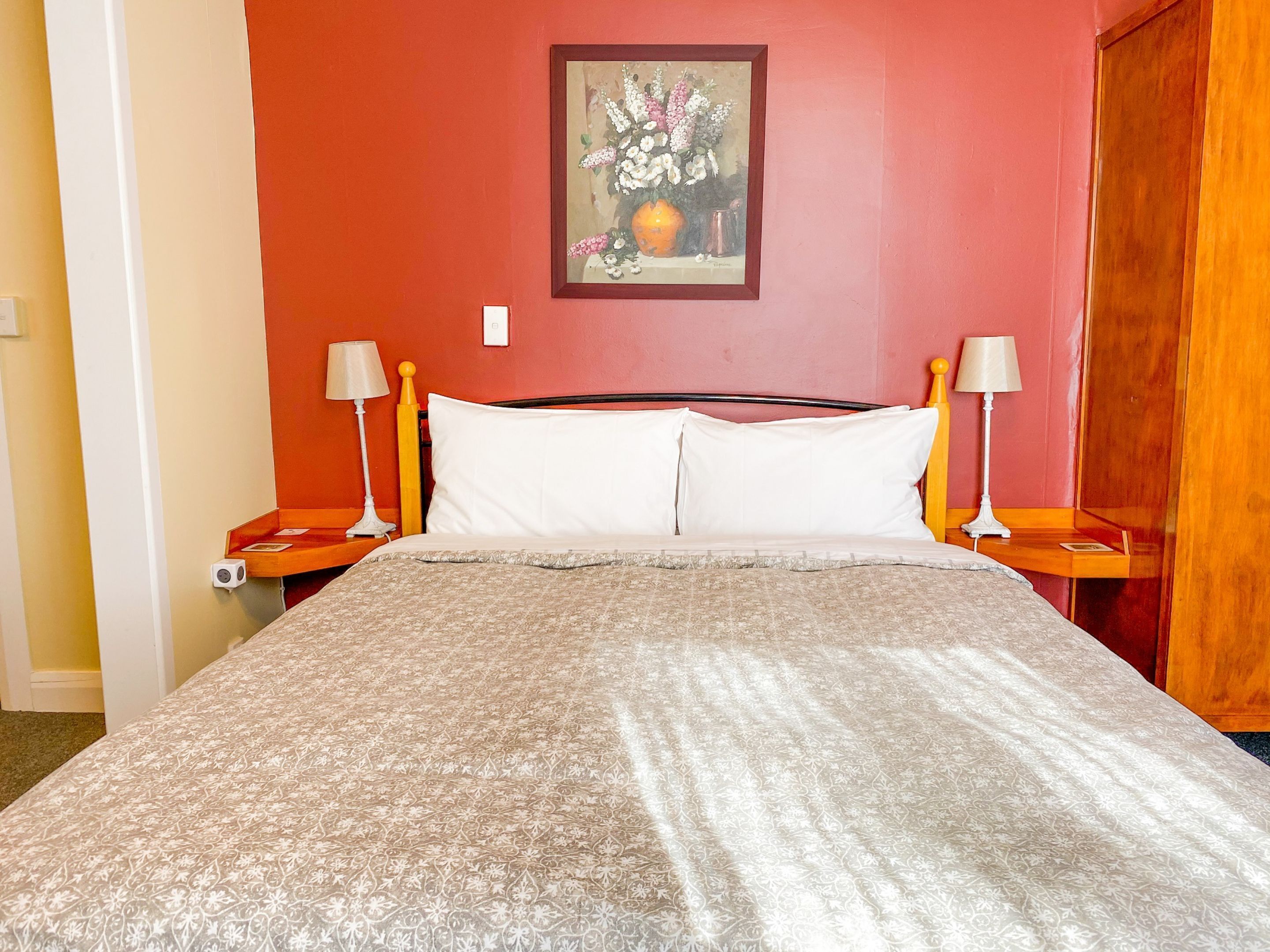 Quarto de hotel com cama, duas mesas de cabeceira, luminária e um quadro na parede.
