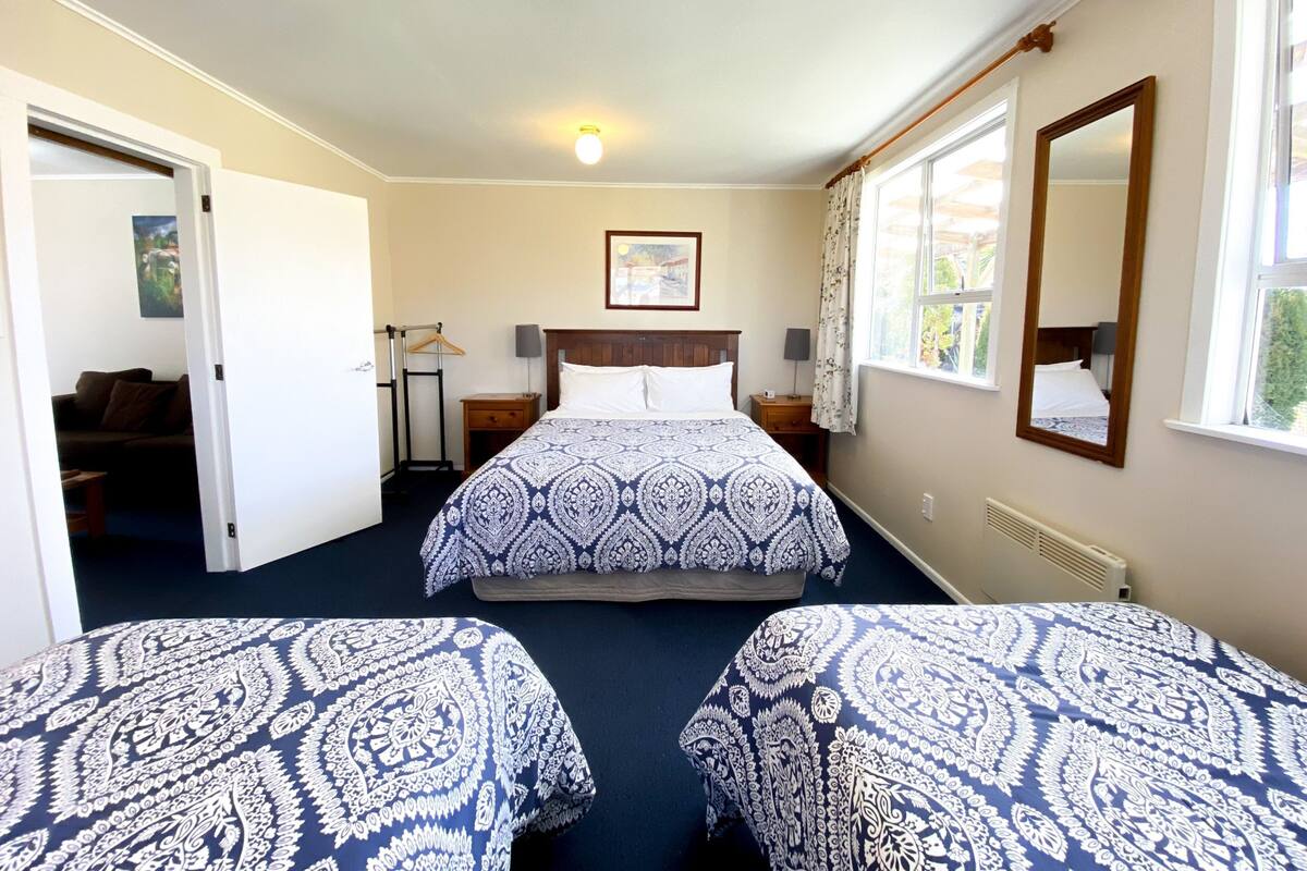 Een hotelkamer met twee bedden, nachtkastjes met lampen, een kapstok, een lijst met een afbeelding aan de muur, en een raam met uitzicht.