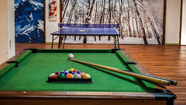 A pool table with a cue stick and balls, a ping pong table, and a winter-themed mural in the background. - Amancay (San Carlos de Bariloche)