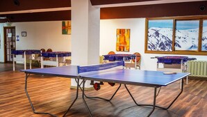 A room with two ping pong tables, wooden flooring, and a large window with a mountain view. - Amancay (San Carlos de Bariloche)