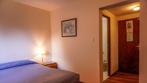 A hotel room with a bed, a nightstand with a lamp, a framed picture on the wall, and a door with a no-smoking sign. - Amancay (San Carlos de Bariloche)