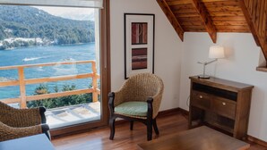 A room with a wooden ceiling, a view of the sea, a wicker chair, a wooden table, and a desk with a lamp. - Amancay (San Carlos de Bariloche)