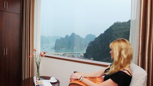 A room with a large window offering a view of a coastal area with boats and greenery. - Ha Long DC Hotel (Hong Gai)