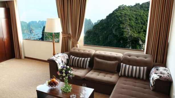 A modern living room with a sofa set, a coffee table with decorative items, and a view of a mountainous landscape through large windows. - Ha Long DC Hotel (Hong Gai)