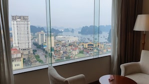 A room with a large window offering a cityscape view, two chairs, and a small table. - Ha Long DC Hotel (Hong Gai)