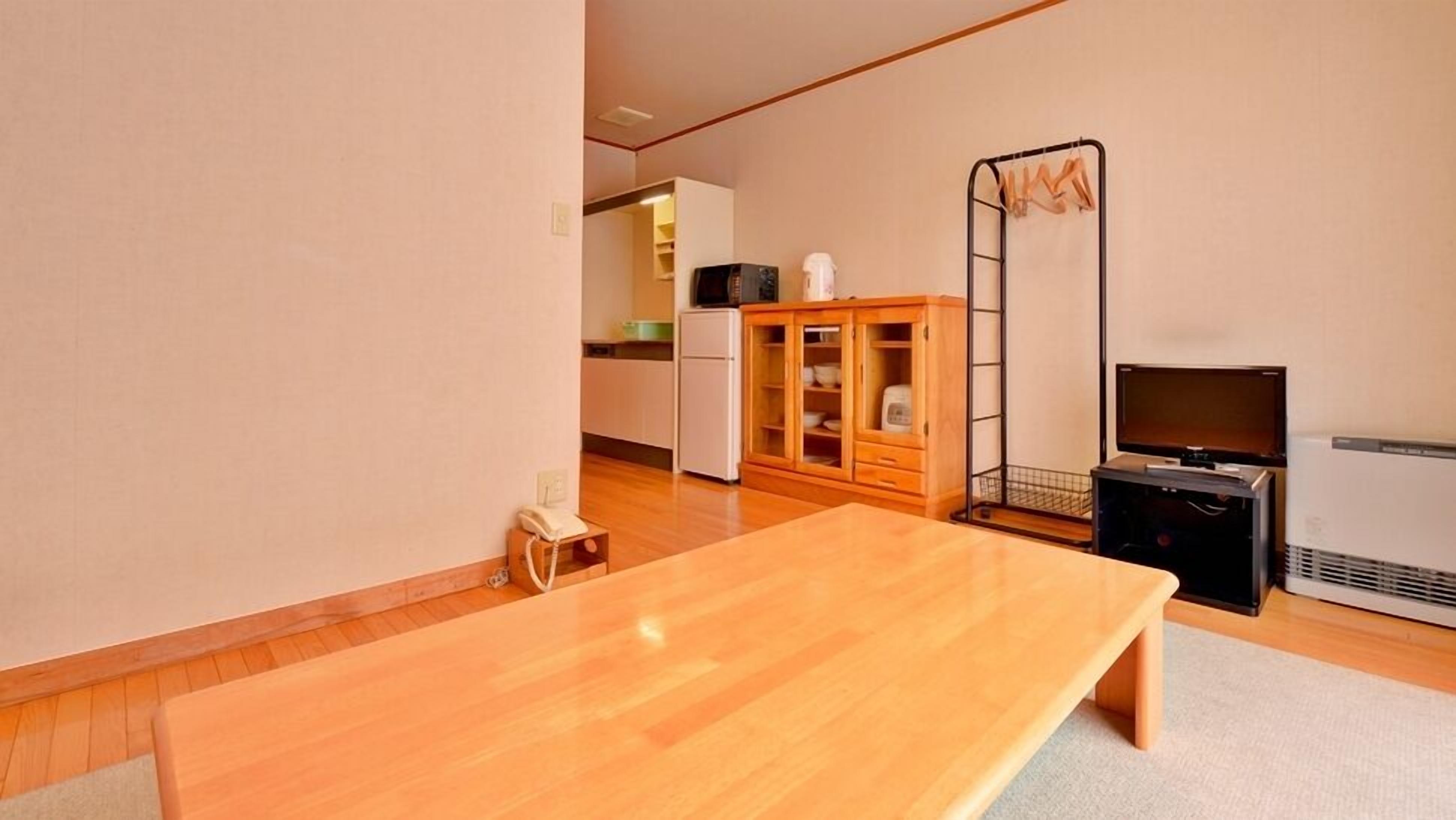 Una habitación con una mesa de madera, un televisor, un armario y una zona de cocina al fondo.