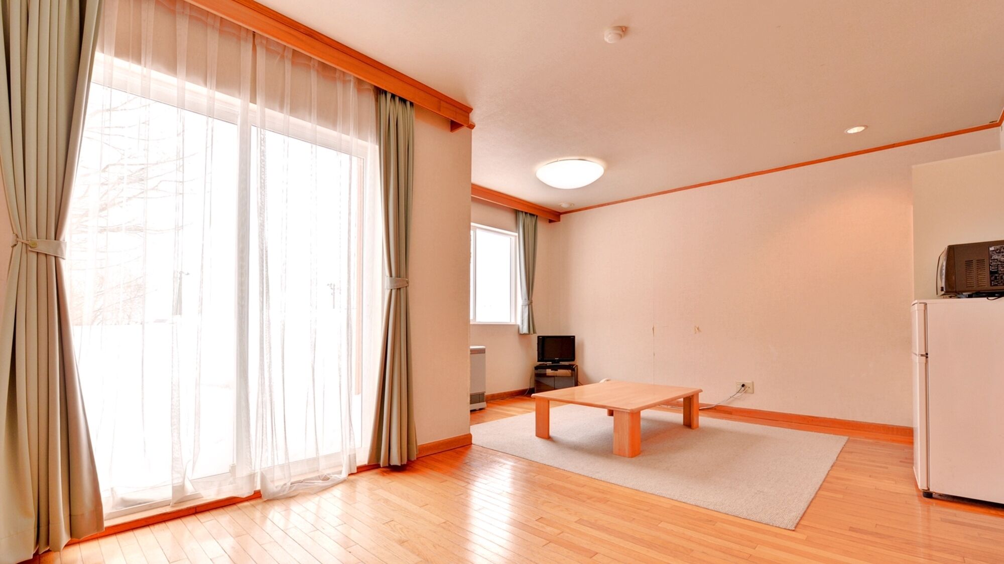Un salón amplio con suelo de madera, una mesa central, un televisor y un refrigerador.