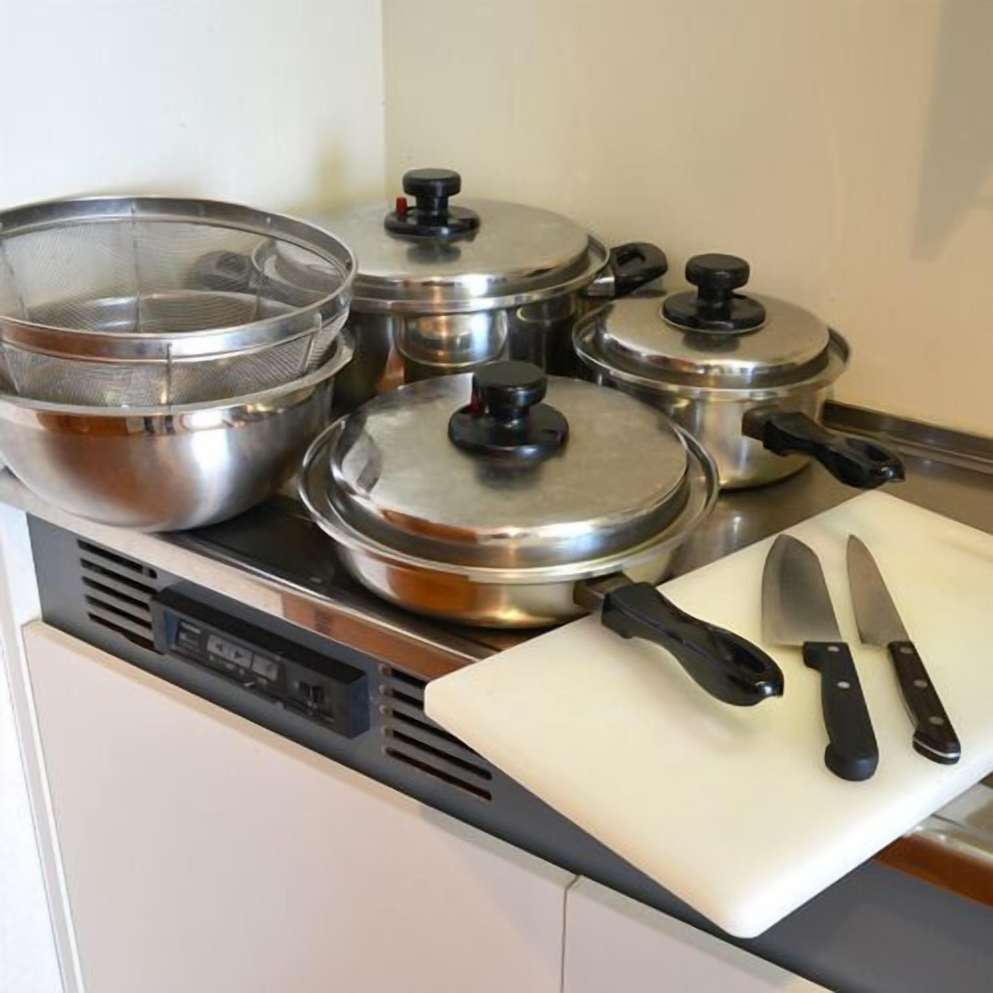 Una cucina con pentole in acciaio inossidabile su un fornello, un tagliere con un coltello e un pannello di controllo digitale.