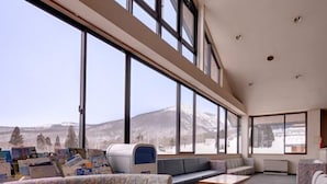 Un interior moderno con ventanas grandes, un sofá modular, una mesita y una fila de sillas.