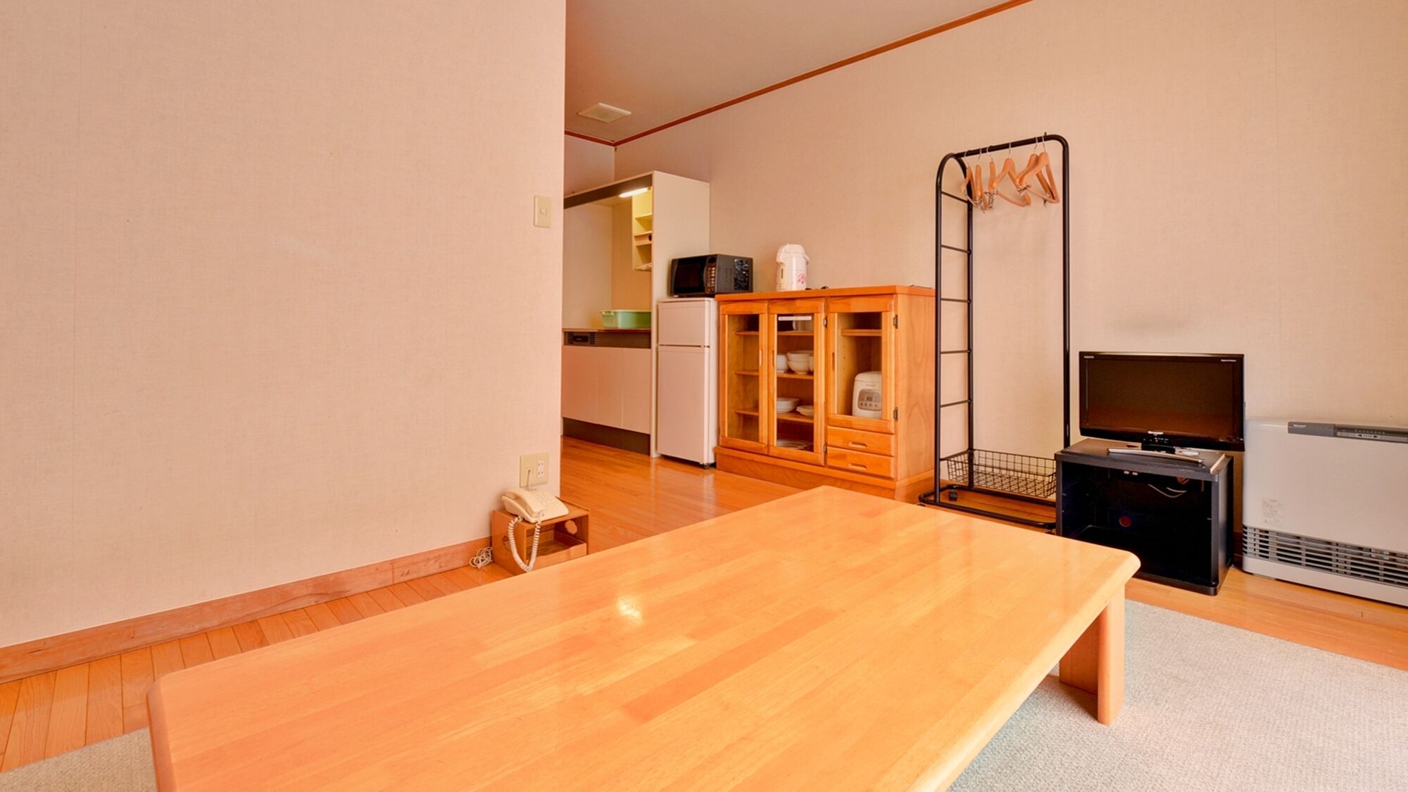 Una habitación con una mesa de madera, televisión, microondas, refrigerador y un armario.