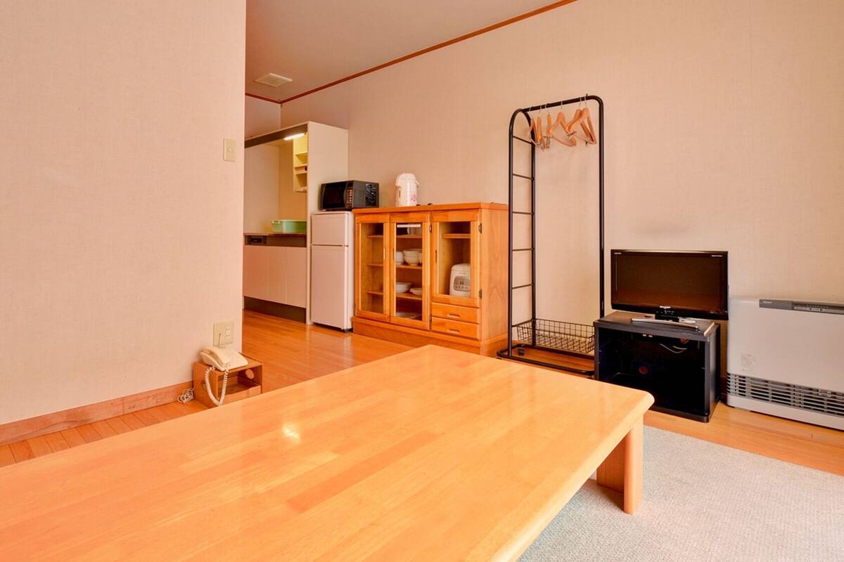 A room with a wooden table, a TV, a microwave, a refrigerator, and a cabinet.
