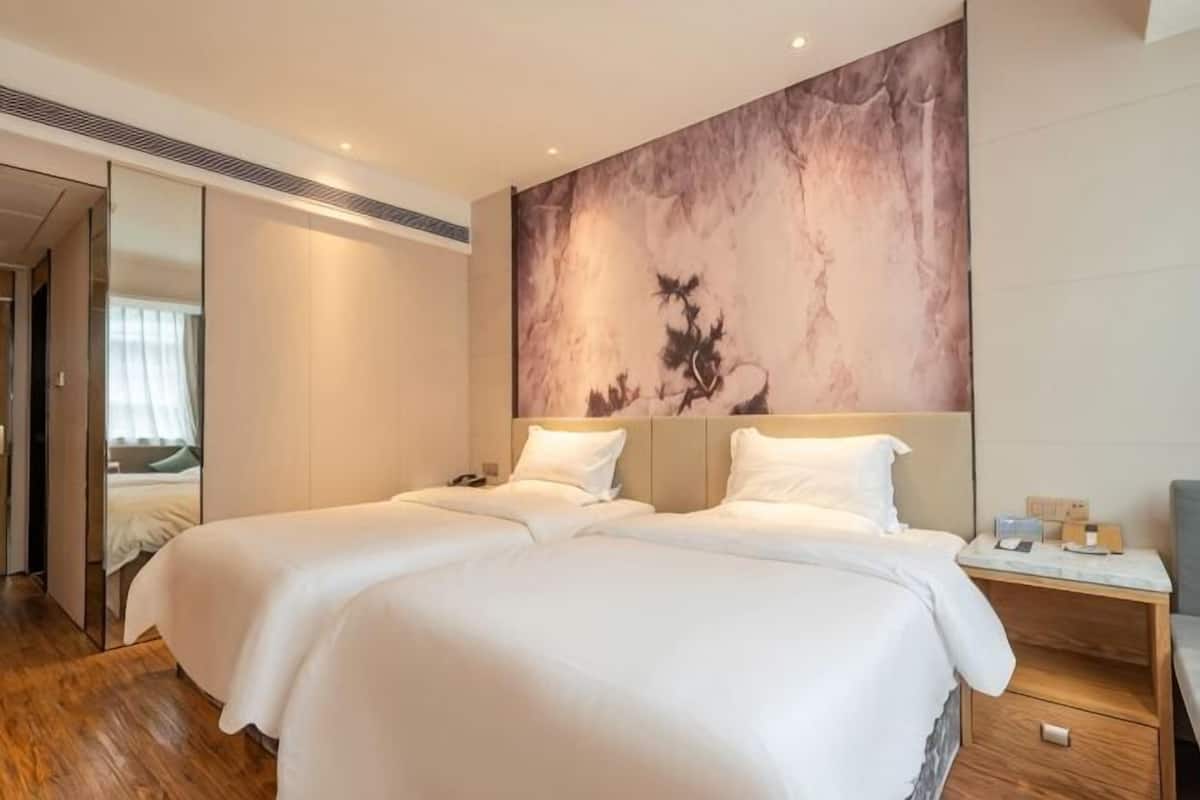 A hotel room with two beds, a large abstract painting on the wall, and a wooden nightstand.
