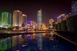 Un paisaje urbano nocturno con edificios iluminados y una superficie acuática reflectante.