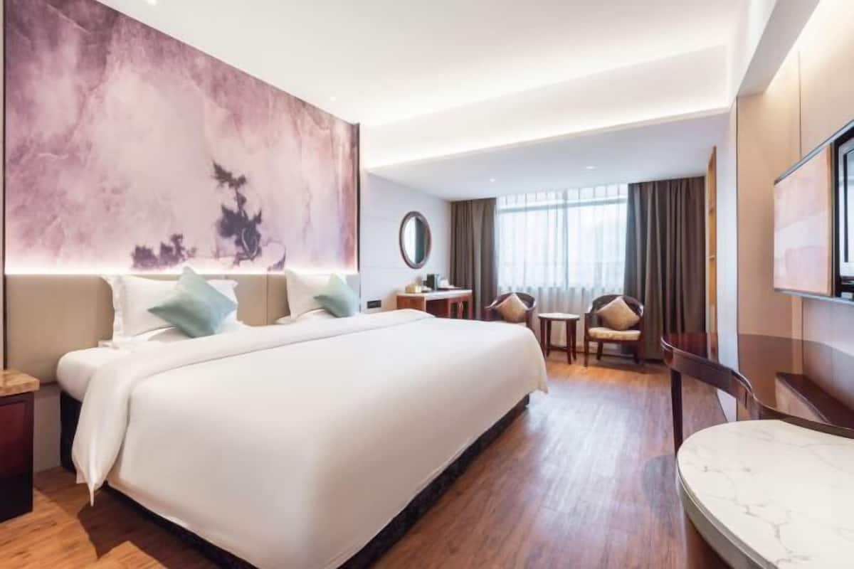 A hotel room with a large bed, a desk, a chair, a TV, and a large abstract painting on the wall.