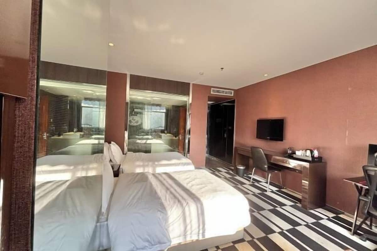A hotel room with two beds, a desk, a chair, a television, and a large mirror.
