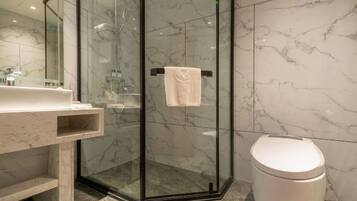 Un baño moderno con ducha envuelta en vidrio, inodoro blanco y pared con azulejos de mármol.