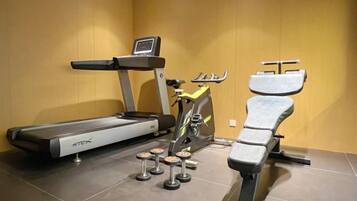 Une salle de sport équipée d’un tapis de course, d’un vélo elliptique et d’un banc de musculation.