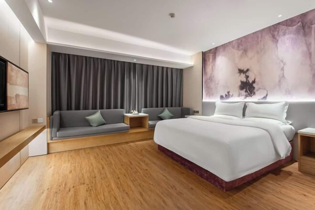 A modern hotel room with a large bed, a sofa, two side tables, and a large abstract painting on the wall.