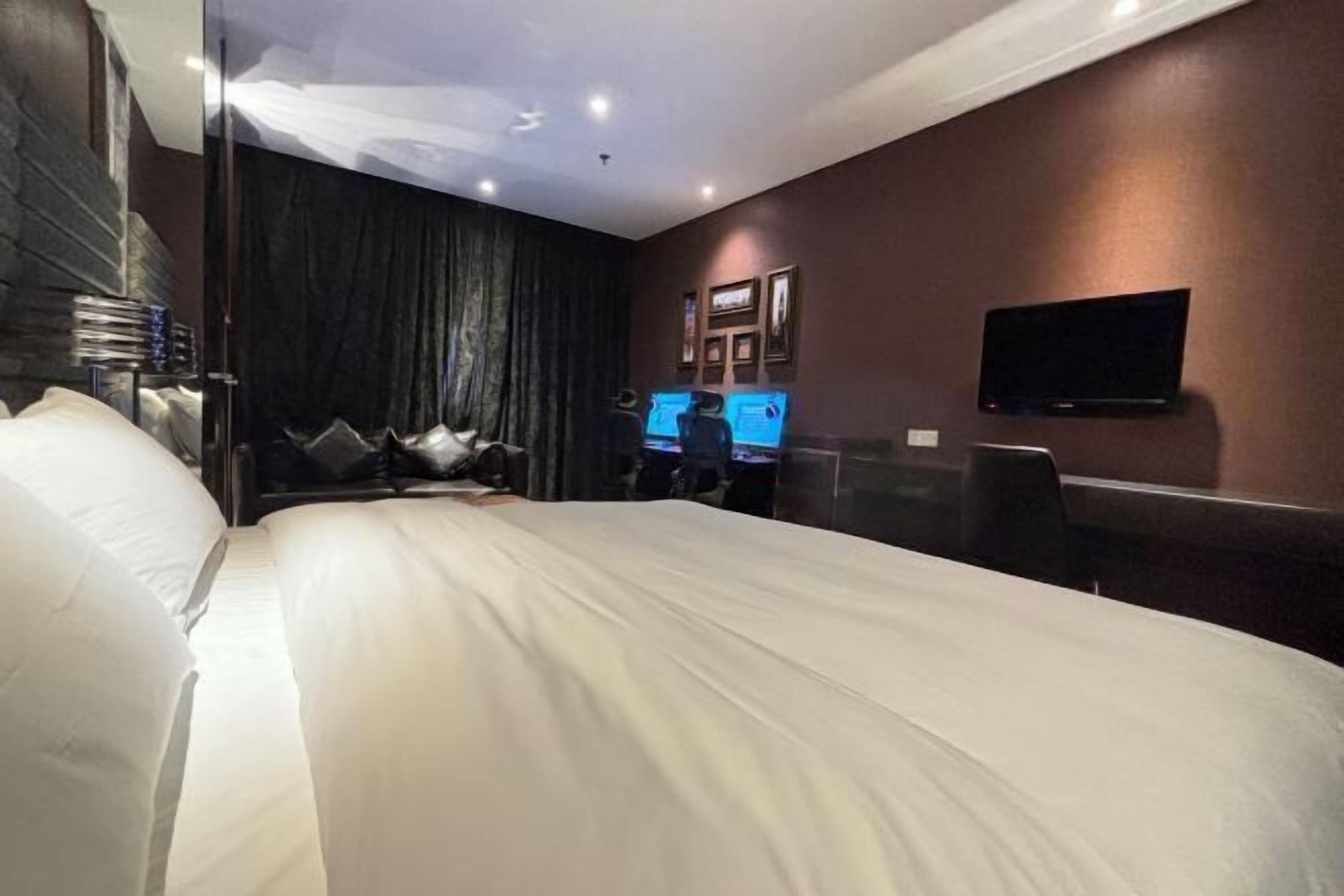 A modern hotel room with a large bed, a flat-screen TV mounted on the wall, and a desk with a computer.