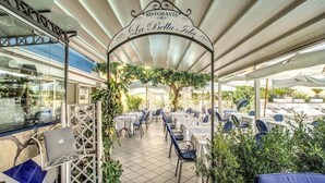 Ein Essbereich im Freien mit Tischen und Stühlen, ein überdachter Gang und ein Schild mit der Aufschrift 'Ristorante La Bella Vita'.