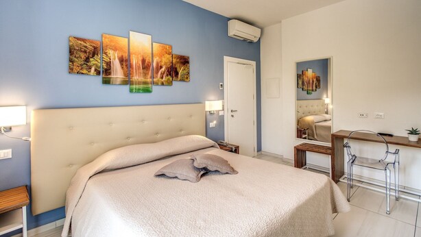 Ein Schlafzimmer mit einem großen Bett, einem Schreibtisch und einem Stuhl. An der Wand befinden sich eine Tür und eine Klimaanlage.