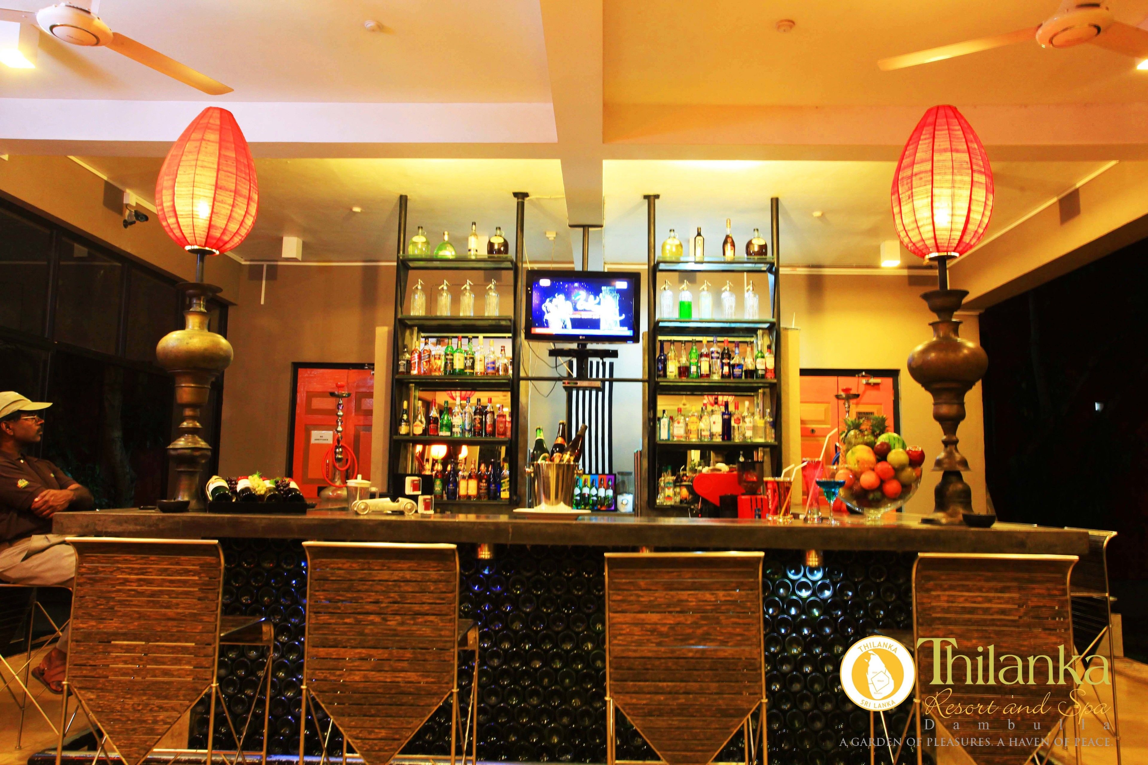 A bar area with a television, shelves of bottles, and two decorative red lamps.