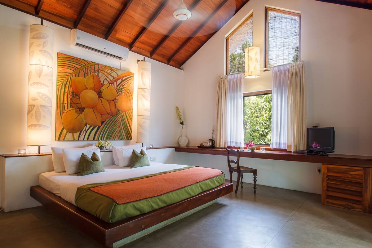 A bedroom with a bed, a desk, a chair, a TV, and a window with curtains.