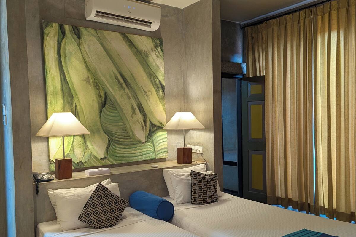 A hotel room with a large bed, two bedside lamps, a wall-mounted air conditioner, and a window with curtains.