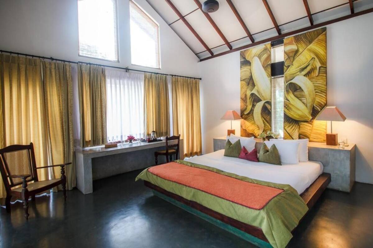 A bedroom with a bed, two bedside lamps, a window with curtains, a desk, and a chair.