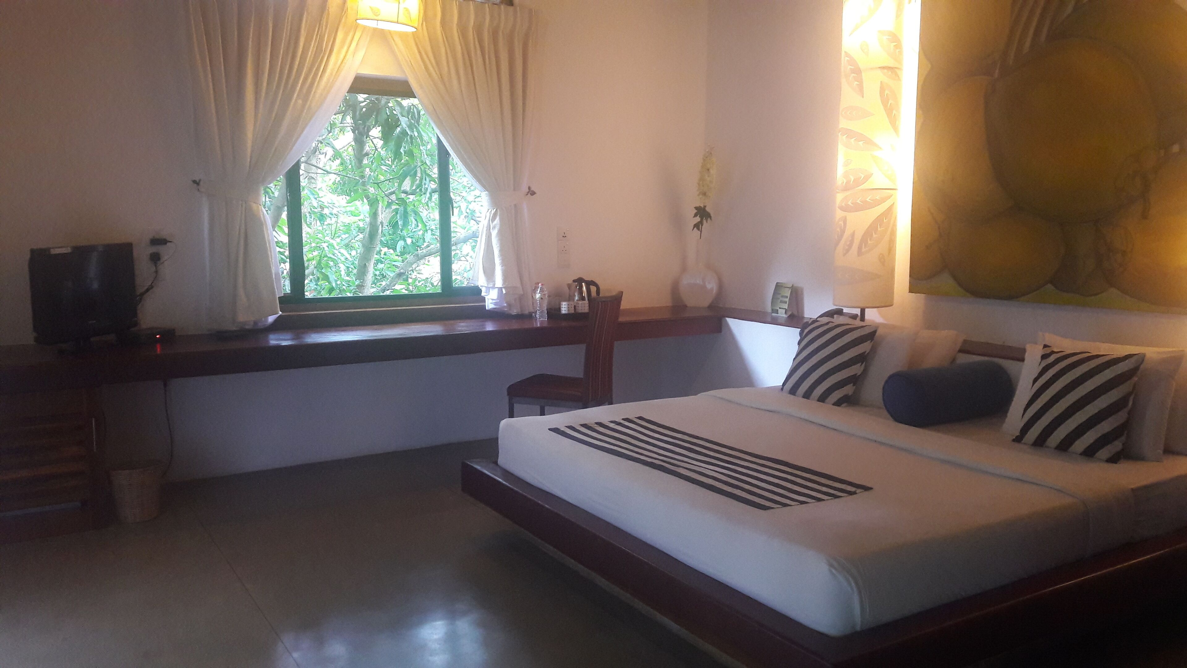 A bedroom with a bed, a desk, a chair, a window with curtains, and a wall-mounted lamp.