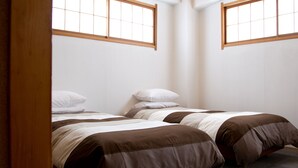 A bedroom with two beds, wooden headboards, and a window with a grid pattern. - Hakuba House (Hakuba)