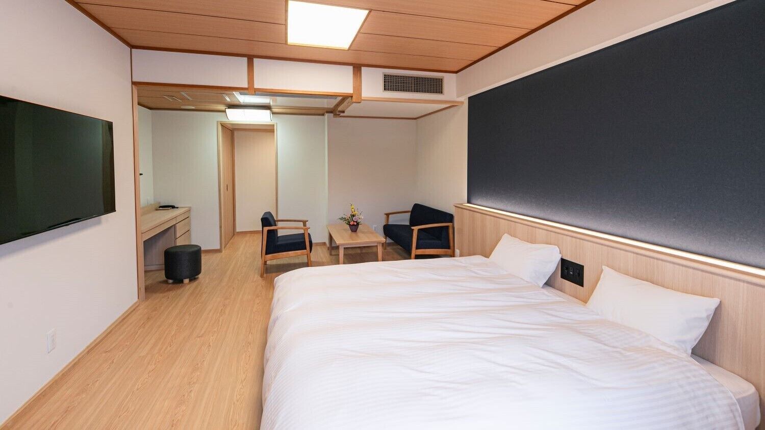 Hotelkamer met een groot bed, een bureau, twee stoelen, een flatscreen televisie en een groot schoolbord aan de muur.