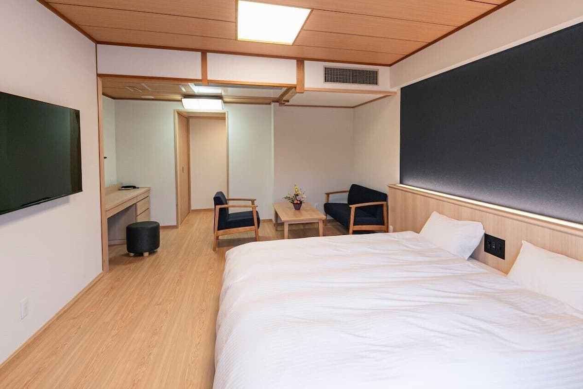 Habitación de hotel con una cama grande, un escritorio, dos sillas, un televisor de pantalla plana y una pizarra grande en la pared.