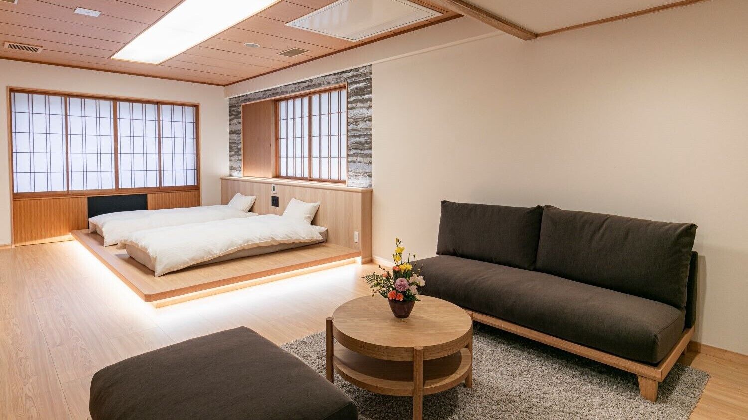 Een moderne kamer met een bed, een bank en een ronde tafel met bloemen.