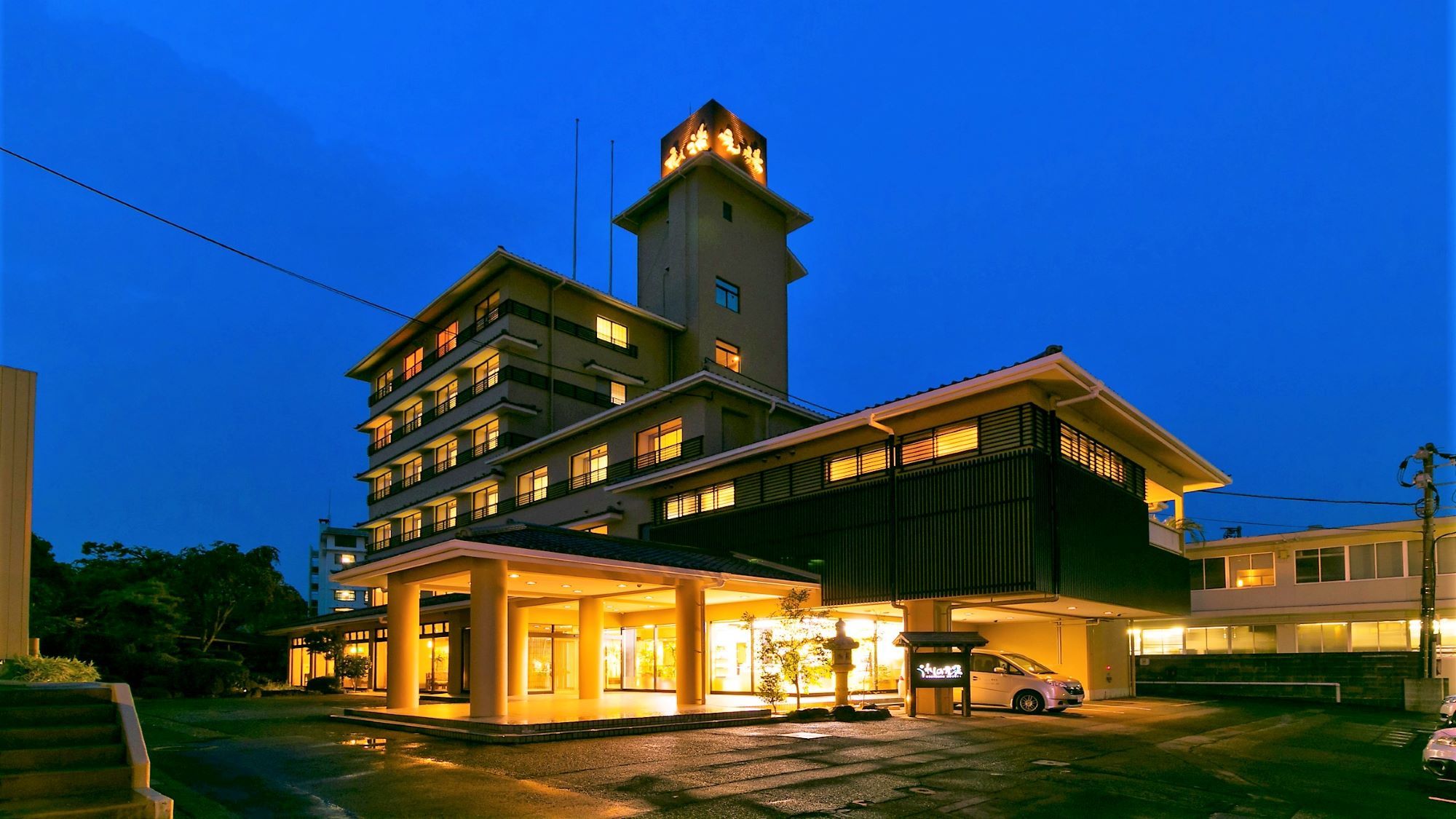 Un hotel de varios pisos con una torre destacada, un acceso cubierto y una zona de estacionamiento.