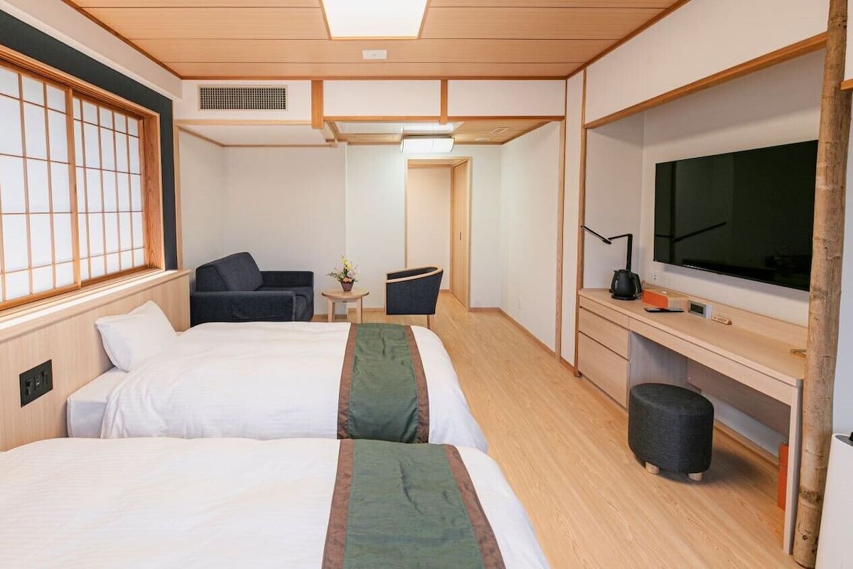 Habitación de hotel con dos camas, un televisor, un escritorio y una mesita con una lámpara.