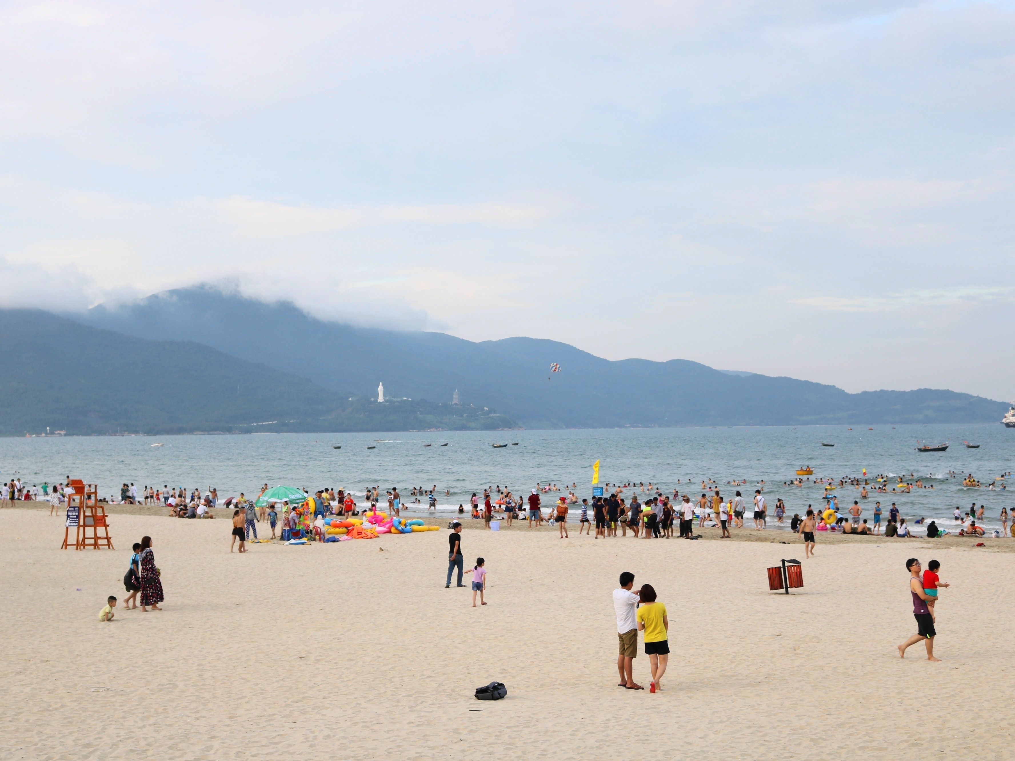 Une plage bondée, avec des gens, des parasols et des bateaux.