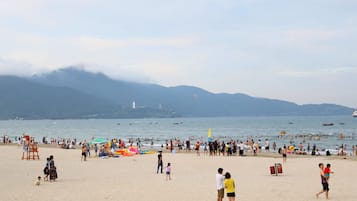 Une plage bondée, avec des gens, des parasols et des bateaux.