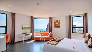 Habitación de hotel moderna con una cama grande, un escritorio, un sofá y vistas a la ciudad y al mar.
