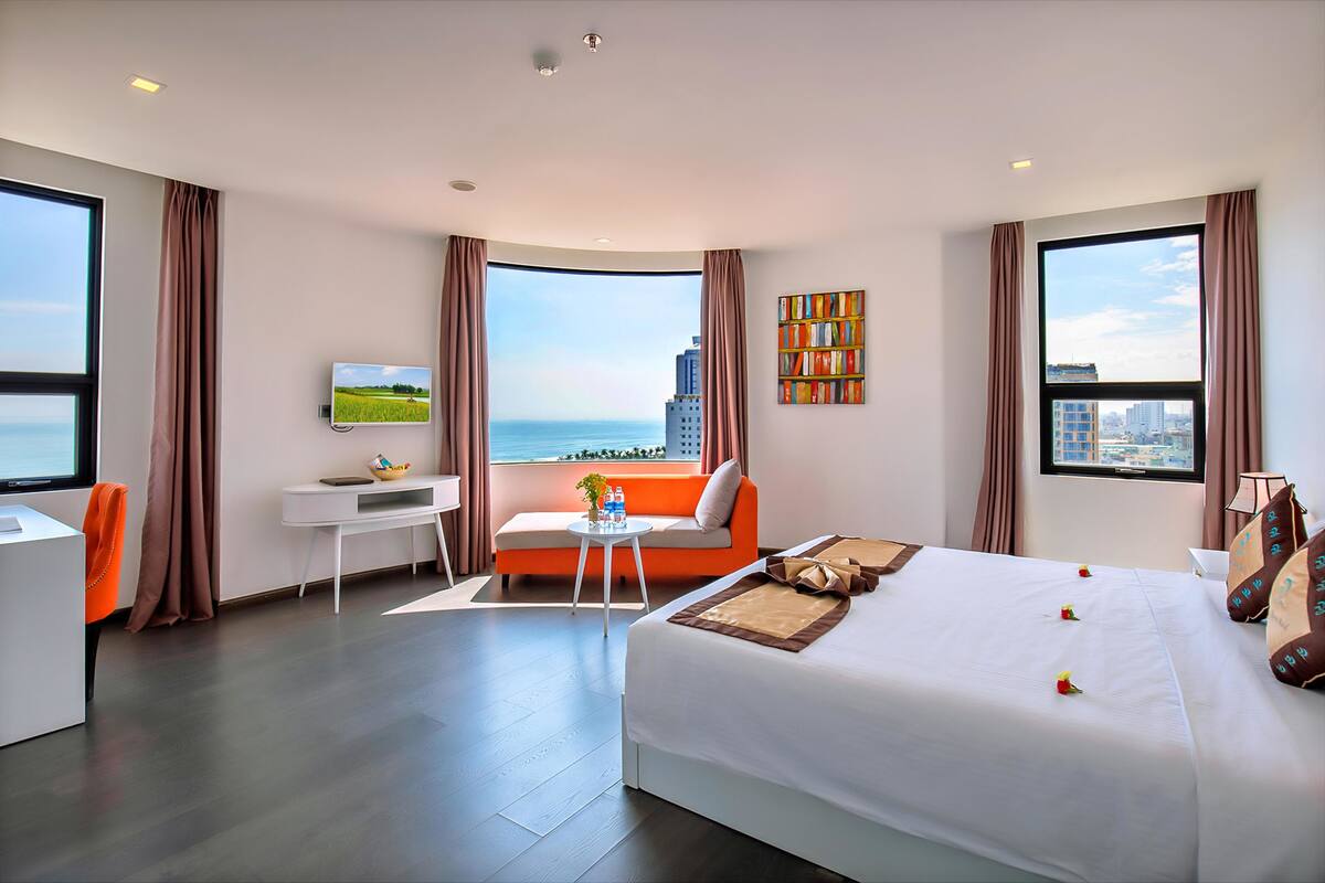 Habitación de hotel moderna con una cama grande, un escritorio, un sofá y vistas a la ciudad y al mar.