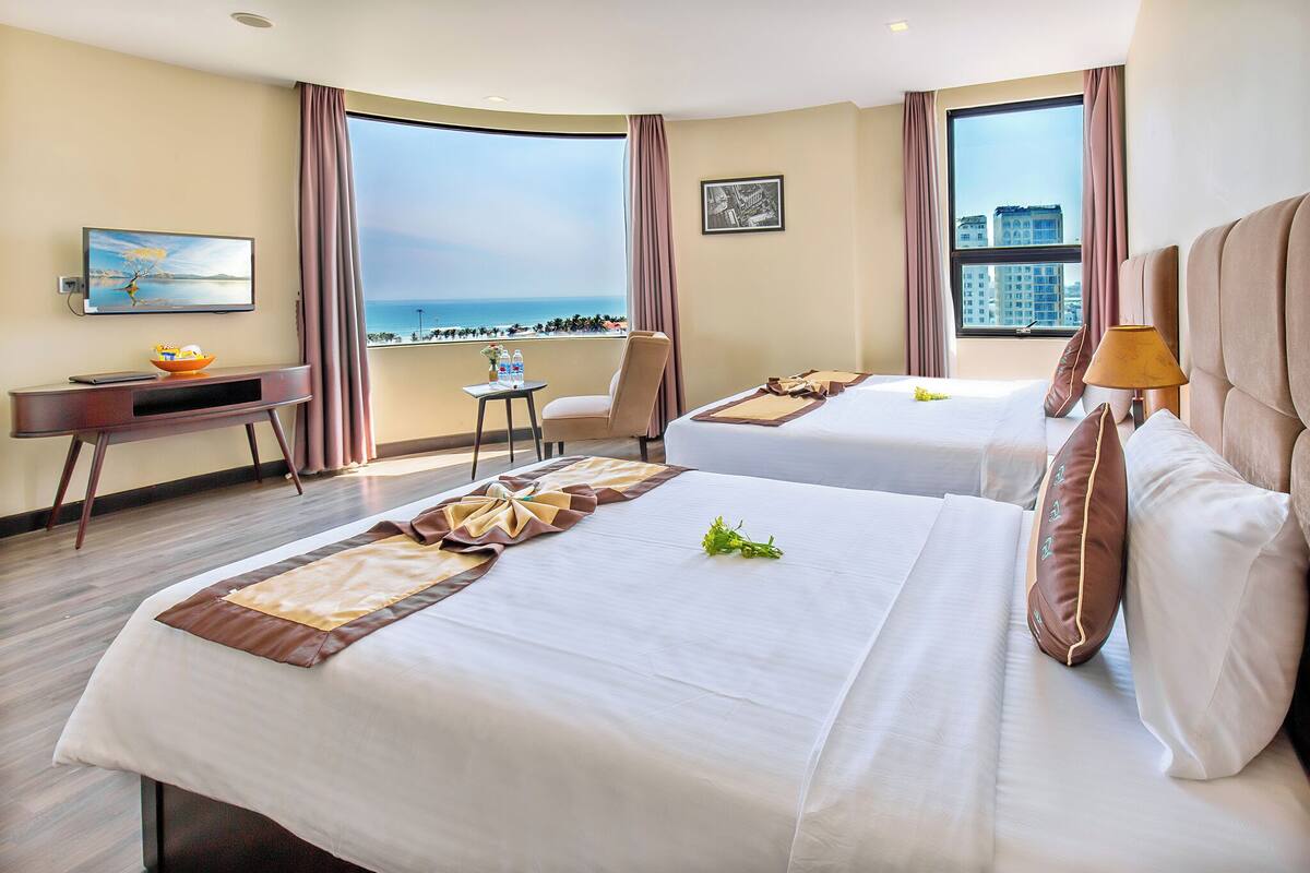 Habitación de hotel con dos camas, un escritorio, una silla y vista al océano.