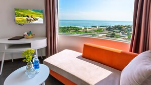 Habitación de hotel moderna con un amplio ventanal que ofrece vista al mar y un paisaje urbano distante.
