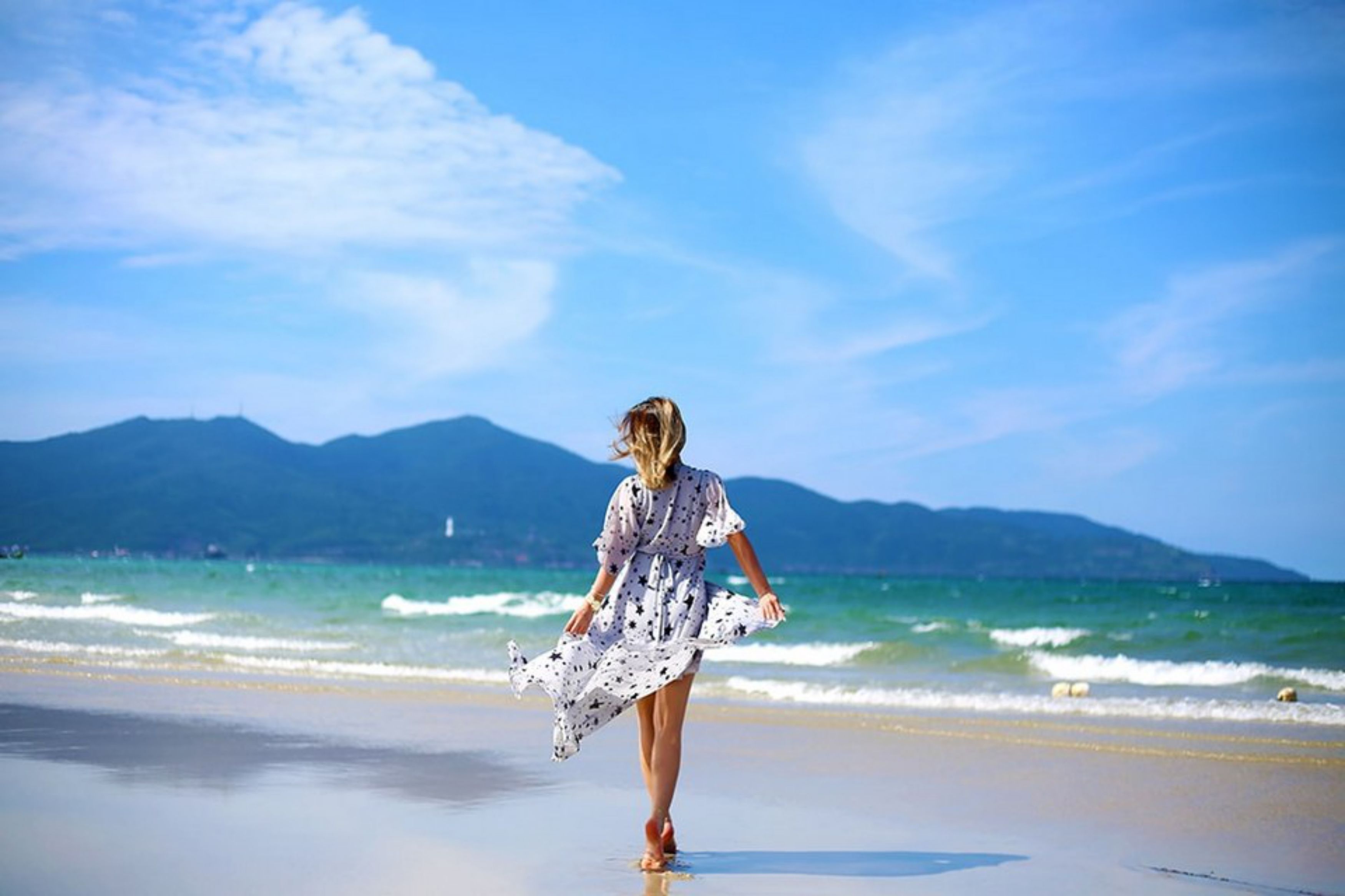 A woman walking on a beach with mountains in the background.