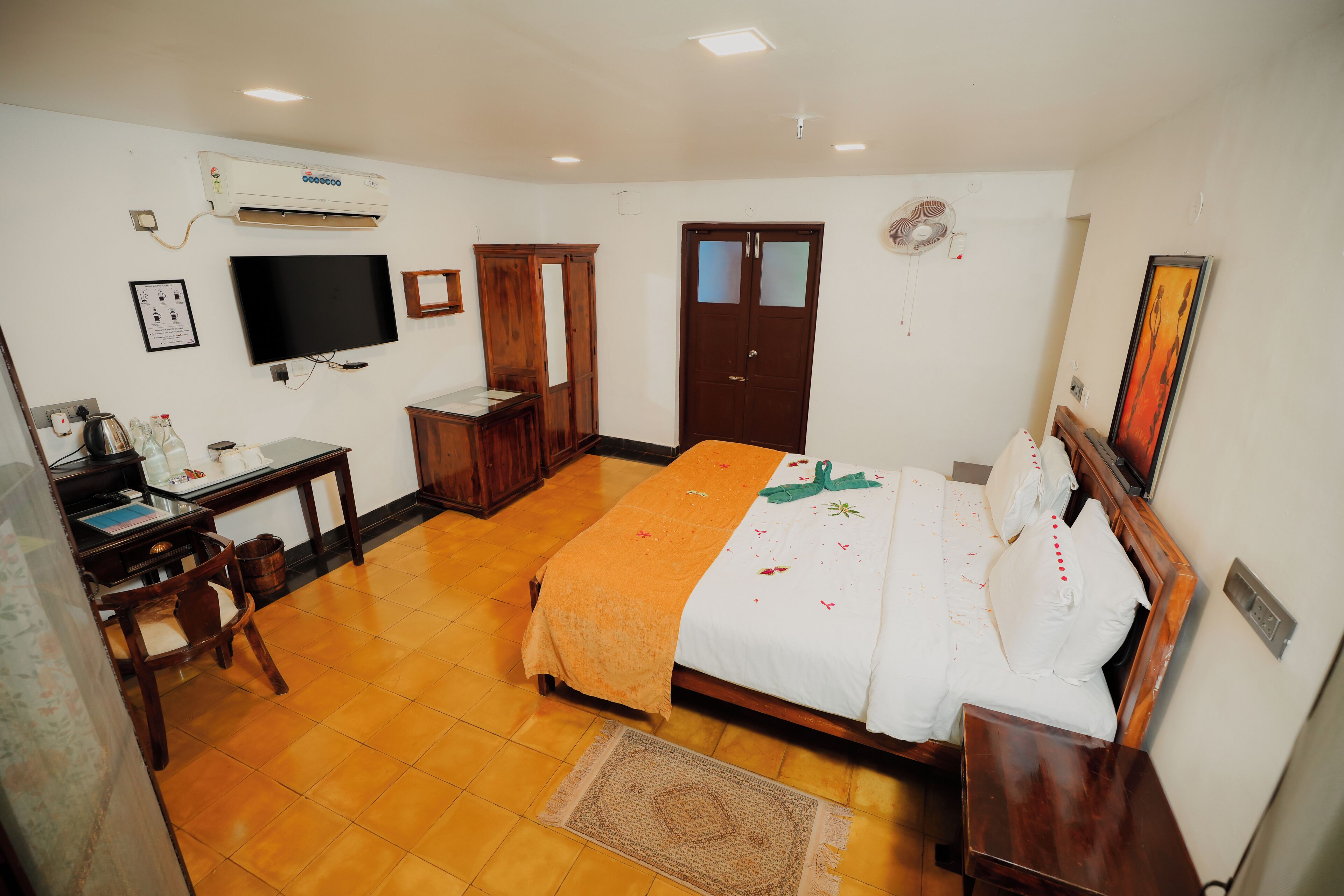 Um quarto com uma cama, escrivaninha, cadeira, televisão e guarda-roupa.