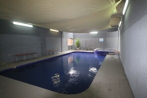 Une piscine intérieure avec des bancs le long des bords, un jacuzzi et une plante en pot.