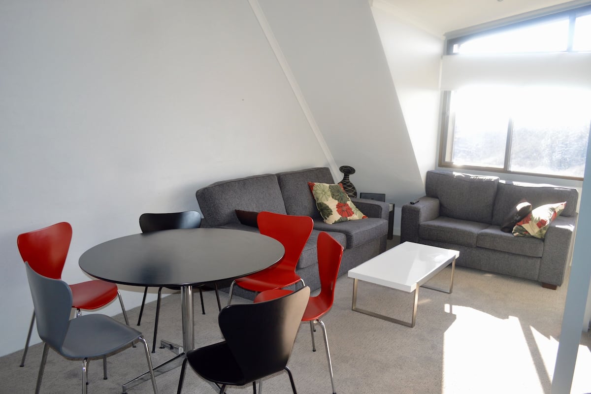 A modern living room with a grey sofa, red and black chairs, a round table, and a white coffee table.